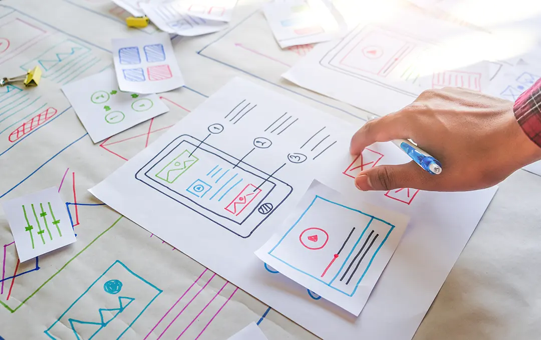 Hand ordnet Skizzen farbiger Website-Layouts auf Papier an.